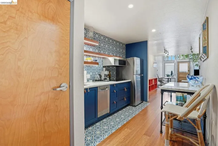 Compact kitchen featuring blue cabinetry with leather pulls, stainless steel appliances, and a patterned tile backsplash