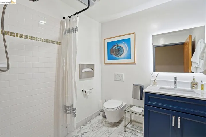 Bathroom featuring a blue vanity with a quartz countertop, an illuminated mirror, and marble-finish flooring