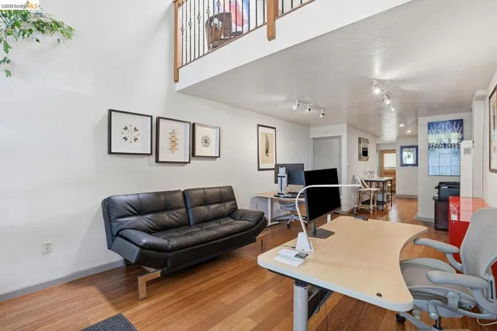 Open-concept space featuring wood-finish flooring, high ceilings, track lighting, and a second-level balcony with a wooden railing