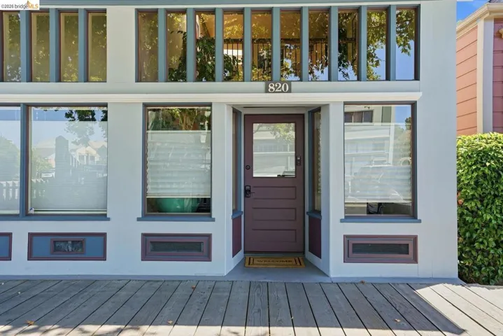 Exterior facade featuring a paneled entry door, multiple windows with transom details, and a wide wood-finish porch