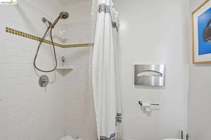 Shower with white subway tile surround, mosaic tile accent band, handheld shower fixture, and corner shelf