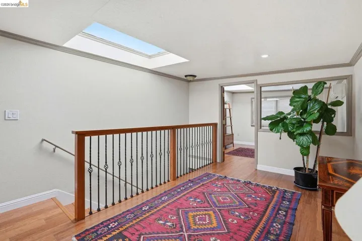 Upper landing featuring a skylight, wood-finish flooring, and a staircase with a wood handrail and wrought iron balusters