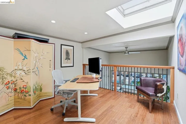 Upper-level loft space featuring wood-finish flooring, a skylight, recessed lighting, and a wood and wrought iron railing overlooking the lower level