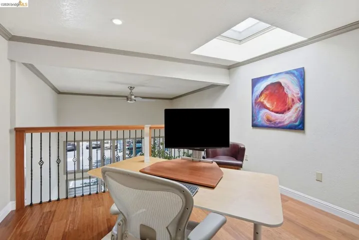 Loft area featuring wood-finish flooring, a skylight, and a ceiling fan