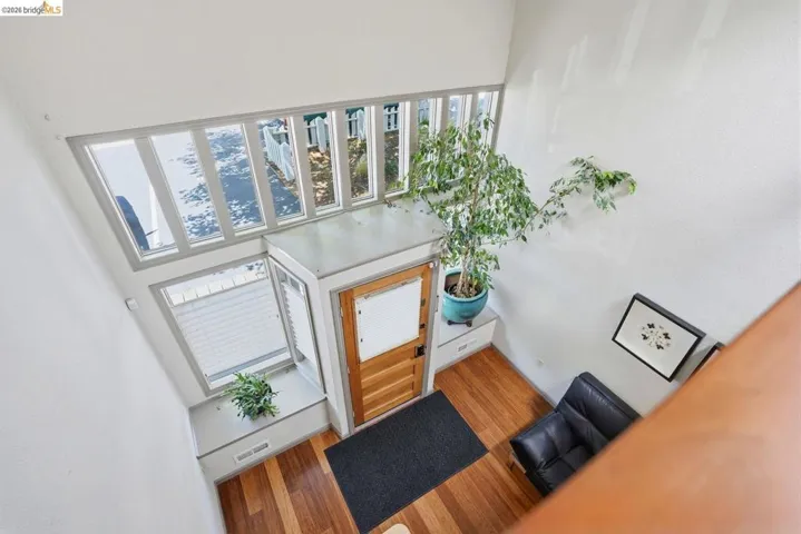 Entryway featuring a double-height ceiling, abundant natural light from upper windows, wood-finish flooring, and a solid wood entry door