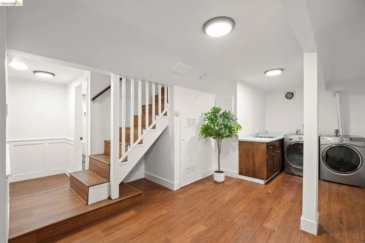 Laundry area featuring a utility sink with a stone-finish countertop, wood-finish cabinetry, and wood-finish flooring