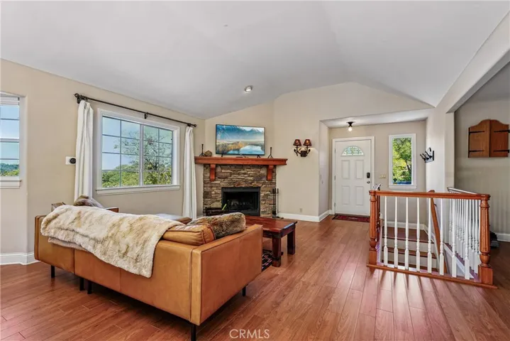 Open living room with vaulted ceiling lines, stone fireplace, warm flooring, large windows, and a comfortable layout designed for mountain gatherings.