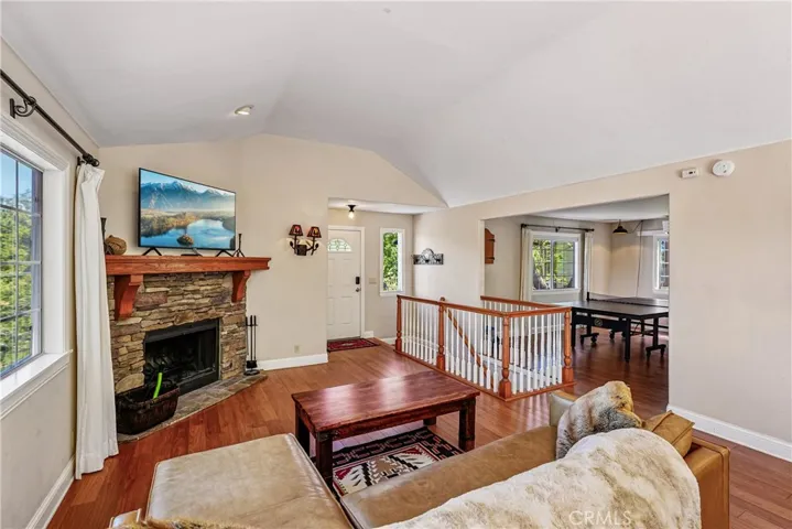 Living room and entry view showing the stone fireplace, open railing, vaulted ceiling, wood-style flooring, and connected flow into the adjacent flex space.