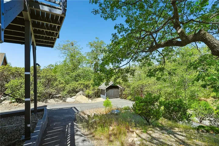 Driveway and natural setting view showing the approach to the home, mature trees, nearby storage structure, and peaceful mountain surroundings.