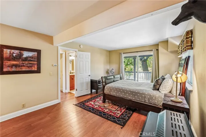 Bedroom with deck access, wood-style flooring, warm natural light, and a relaxed mountain retreat feel close to the adjoining bathroom.