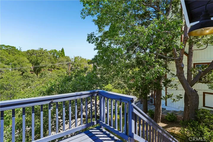Upper deck corner with railing, mature trees, and filtered mountain views, highlighting the home’s outdoor living space and natural surroundings.
