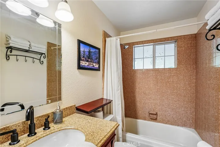 Full bathroom with granite counter, black faucet fixtures, tub-shower surround, and thoughtful mountain-style details including built-in shelving and towel storage.