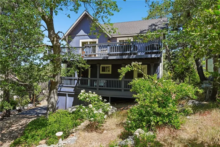 Street-to-home exterior view with mature trees, elevated deck space, driveway access, and natural landscaping in a Lake Arrowhead neighborhood with lake rights.