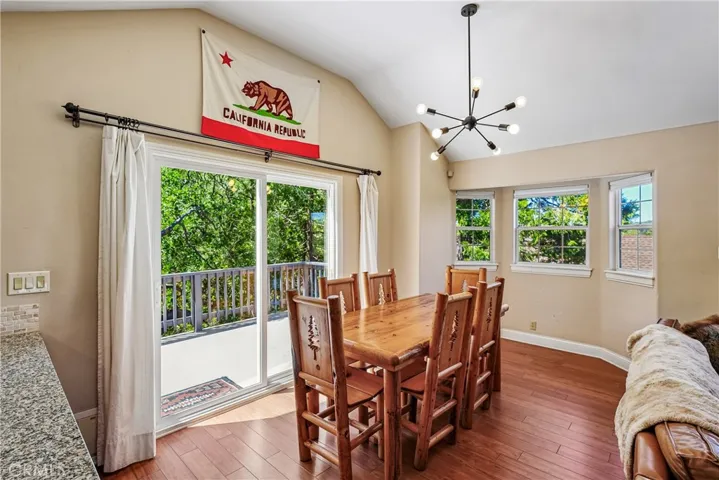 Dining area with vaulted ceilings, sliding glass doors to the deck, warm wood-style flooring, and natural light for relaxed Lake Arrowhead mountain living.