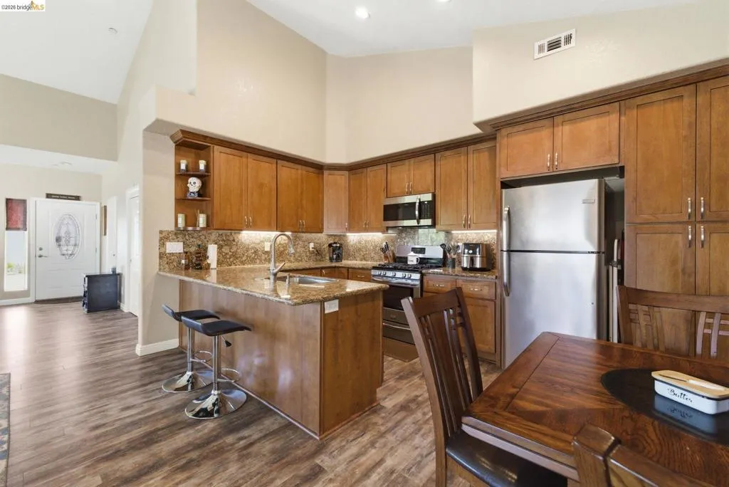 Kitchen with open shelves, a peninsula, dark stone counters, wood finish cabinetry, and stainless steel appliances