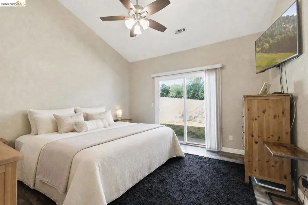 Vaulted ceiling, ceiling fan with integrated lighting, sliding glass door, and wood-finish flooring