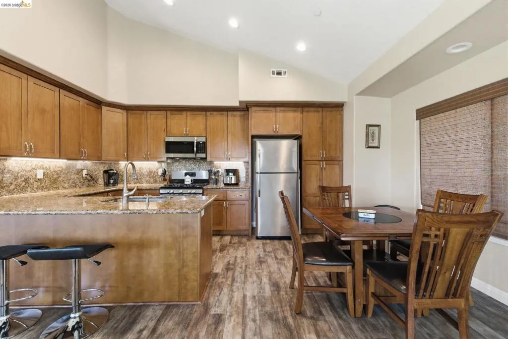 Kitchen with wood finish cabinetry, light stone countertops, lofted ceiling, stainless steel appliances, and a peninsula