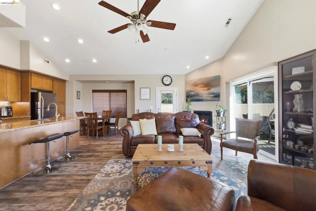 Living room with vaulted ceiling, dark wood-style flooring, a glass covered fireplace, a ceiling fan, and recessed lighting