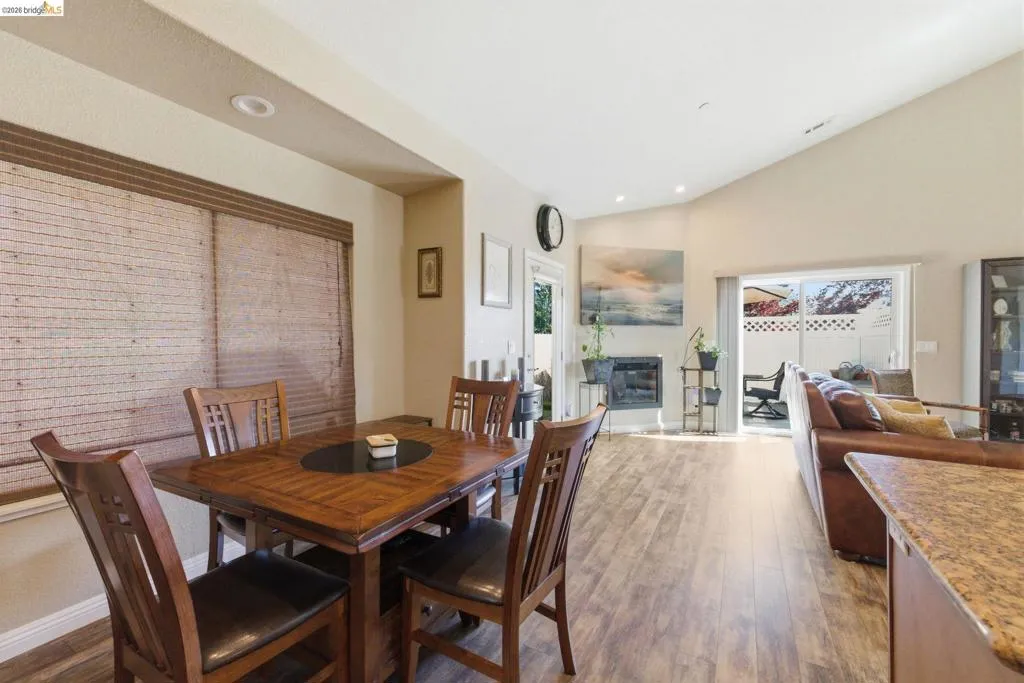 Dining space featuring dark wood-style flooring, vaulted ceiling, a glass covered fireplace, and recessed lighting