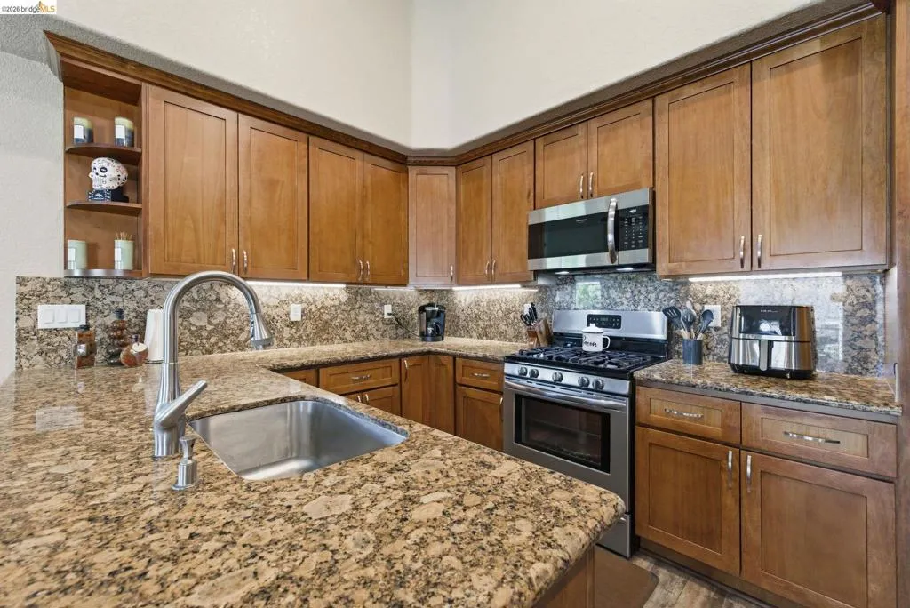 Kitchen featuring stainless steel appliances, wood finish cabinetry, light stone countertops, and open shelves