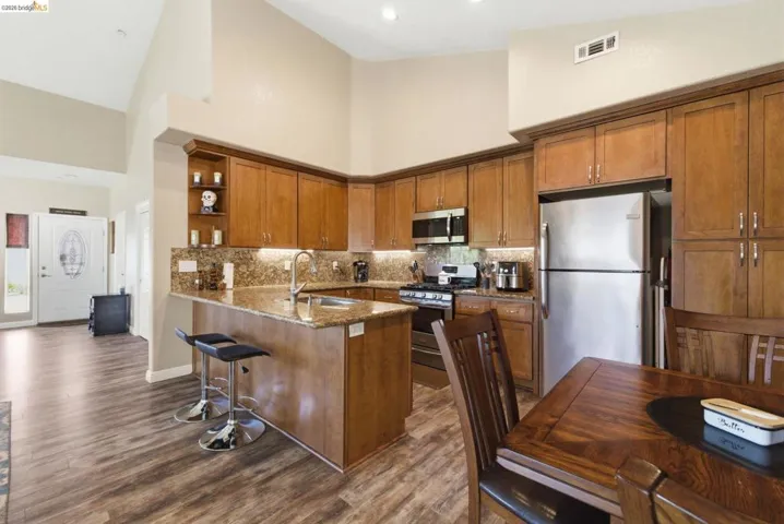 Kitchen with open shelves, a peninsula, dark stone counters, wood finish cabinetry, and stainless steel appliances