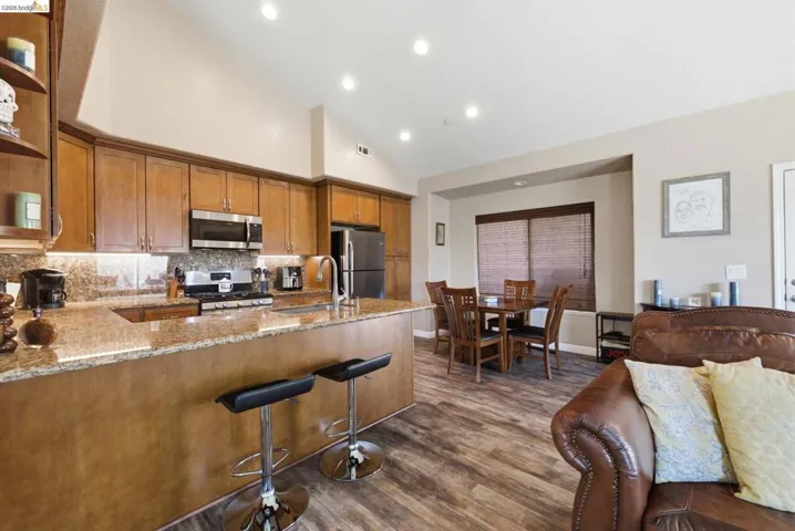Kitchen with light stone counters, wood finish cabinetry, lofted ceiling, a peninsula, and stainless steel appliances