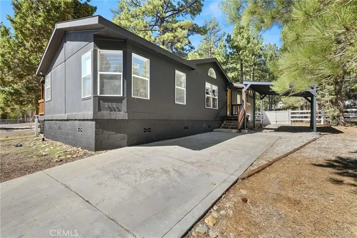 Move-in-ready Big Bear home with all-one-level living, level driveway access, covered entry, carport parking, and a clean mountain-modern exterior surrounded by mature pines.