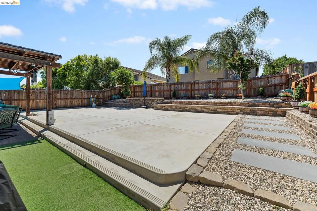 Expansive concrete patio with tiered retaining walls, artificial turf, and a wood pergola