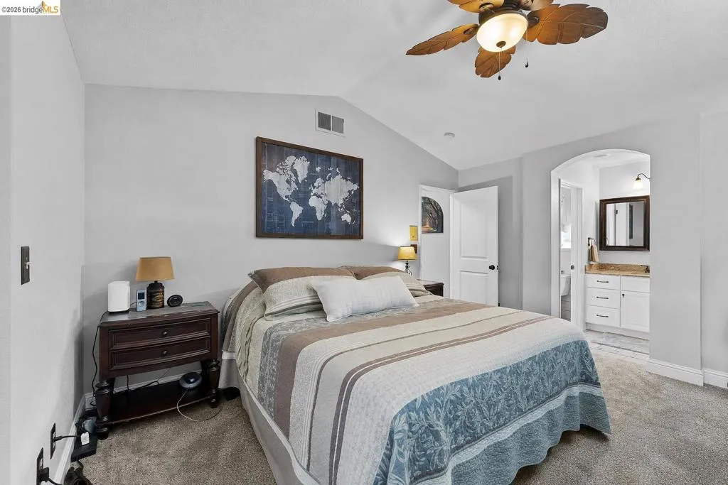 Carpeted bedroom with a vaulted ceiling and a wood-bladed ceiling fan