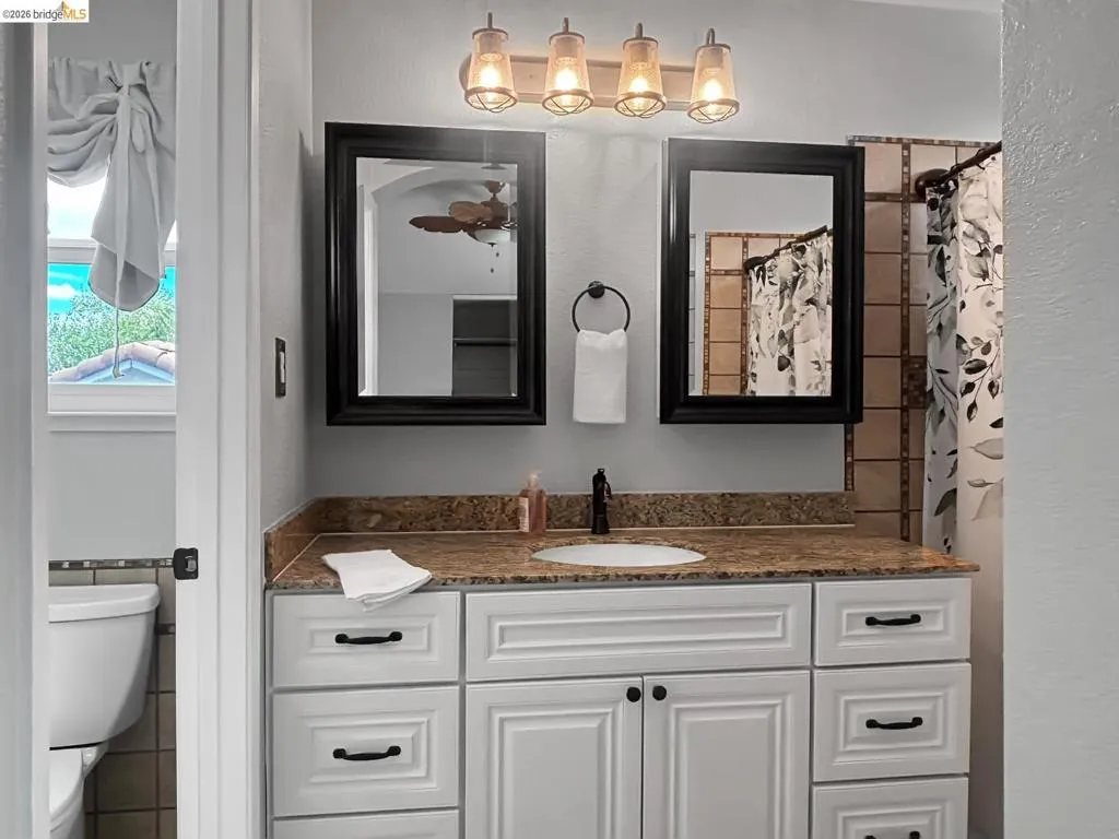 Bathroom vanity featuring a granite countertop with an undermount sink, white cabinetry with black hardware, and two framed mirrors
