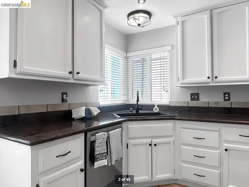 Kitchen featuring white cabinetry with dark hardware, dark countertops, and a dark tile backsplash