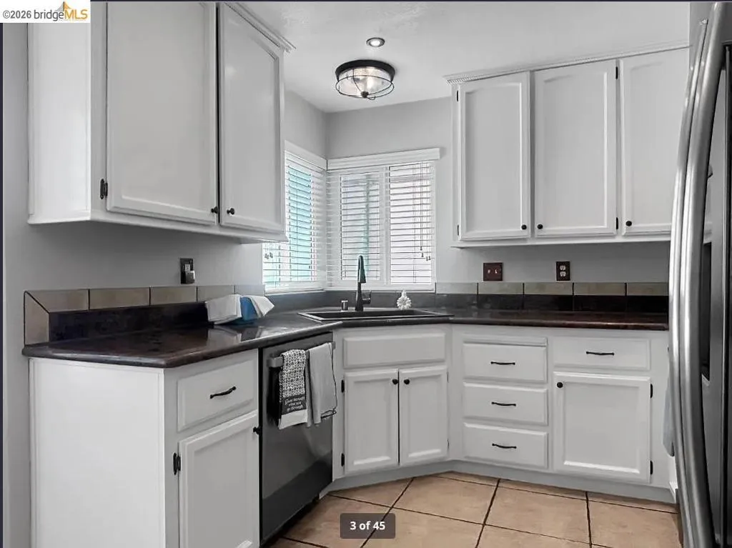 Corner kitchen featuring white cabinetry, dark countertops, and a tile backsplash
