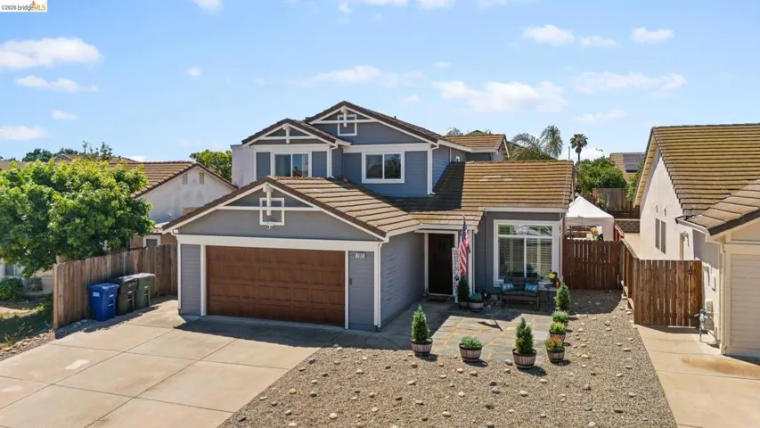 Two-story residence featuring light gray siding with white trim, a brown tile roof, and a two-car garage with a wood-finish door