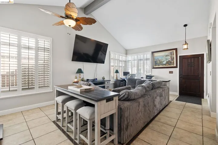 Living area featuring high vaulted ceilings, tile flooring, plantation shutters, a decorative ceiling fan, and a wood-paneled entry door