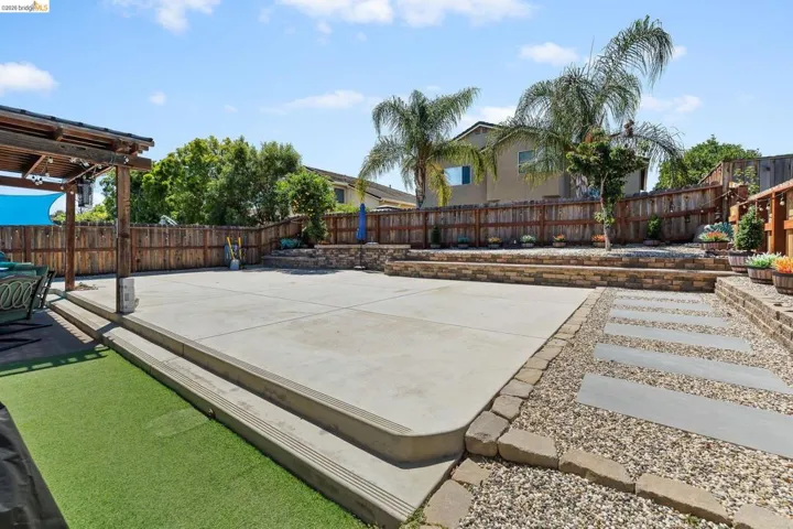 Expansive concrete patio with tiered retaining walls, artificial turf, and a wood pergola