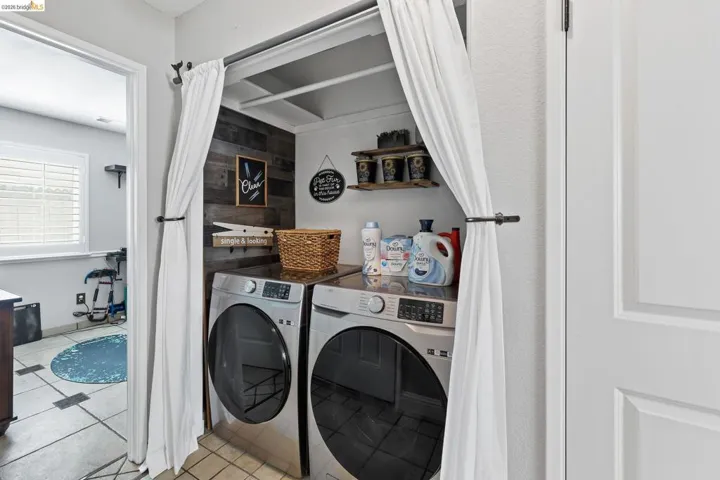 Dedicated laundry area featuring a wood-finish accent wall, upper shelving, and tiled flooring