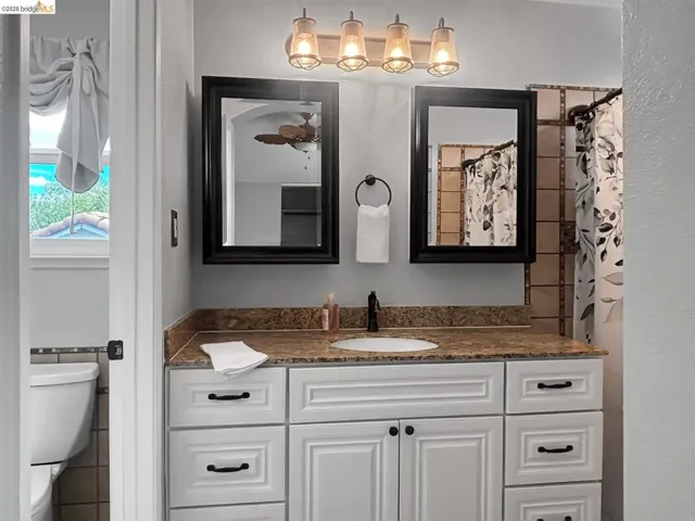 Bathroom vanity featuring a granite countertop with an undermount sink, white cabinetry with black hardware, and two framed mirrors