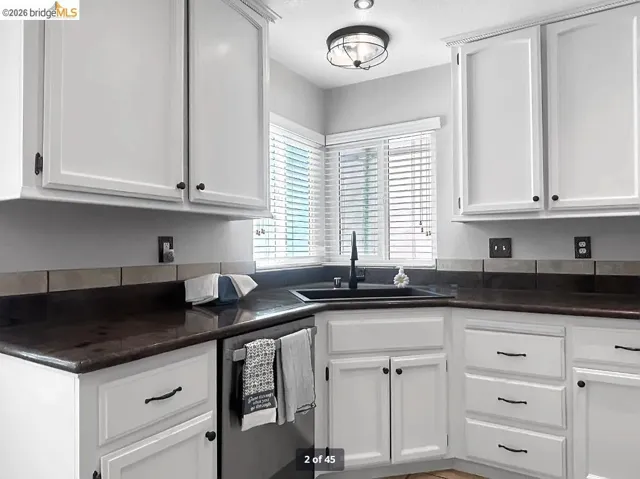 Kitchen featuring white cabinetry with dark hardware, dark countertops, and a dark tile backsplash