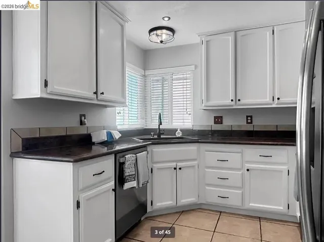 Corner kitchen featuring white cabinetry, dark countertops, and a tile backsplash
