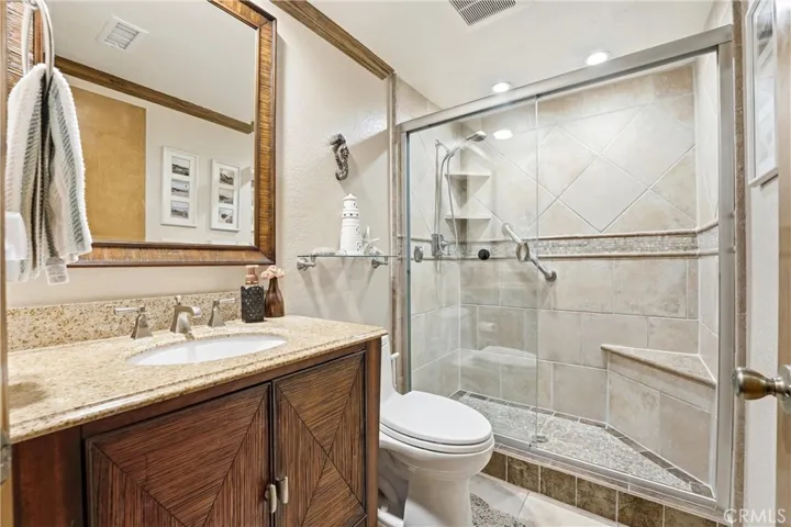 Beautifully updated bathroom featuring a granite-topped vanity, rich wood cabinetry, and a spacious walk-in tiled shower with glass enclosure. Thoughtful finishes and a clean, spa-like design create a relaxing retreat.