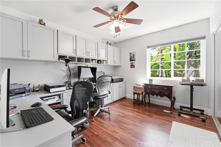 Dedicated home office features extensive custom built-in cabinetry, generous workspace, and warm wood flooring. Large windows frame lush tropical greenery, creating a bright and inspiring environment for working from home.