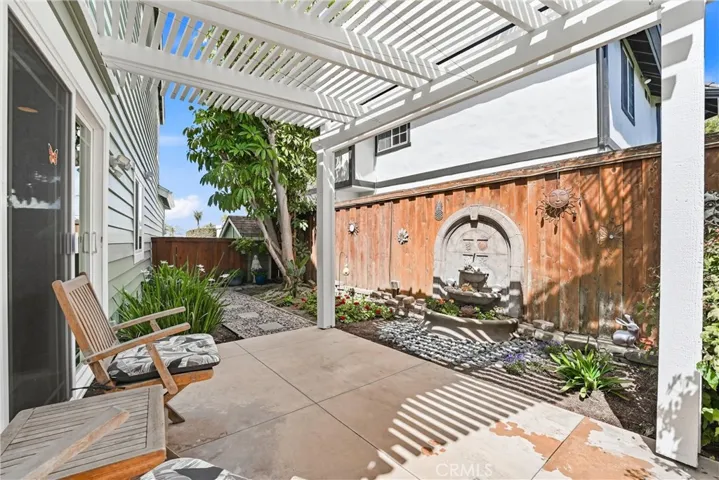 Covered patio with a pergola offers a peaceful outdoor sitting area surrounded by mature landscaping and charming garden details. The shaded space is perfect for enjoying morning coffee or relaxing outdoors year-round.