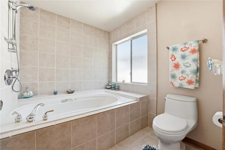 Relaxing primary bath includes a soaking tub surrounded by tile finishes and natural light from a large privacy window. A comfortable space to unwind and recharge.