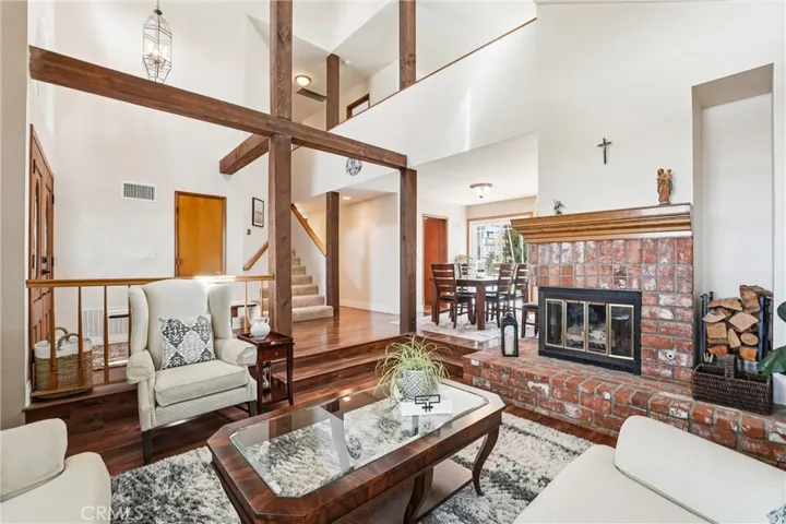 Rich wood flooring, dramatic ceiling height, and a floor-to-ceiling brick fireplace create a warm and welcoming focal point in the main living area.