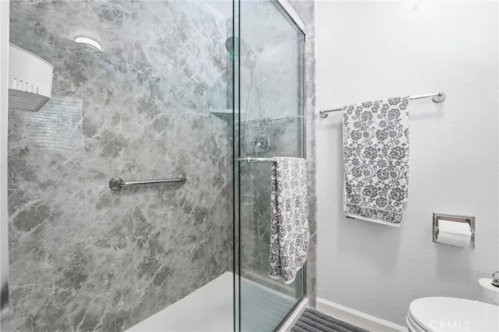 Updated bathroom includes a sleek glass-enclosed shower with elegant stone-inspired wall finishes. Modern fixtures and thoughtful details contribute to the sophisticated feel.