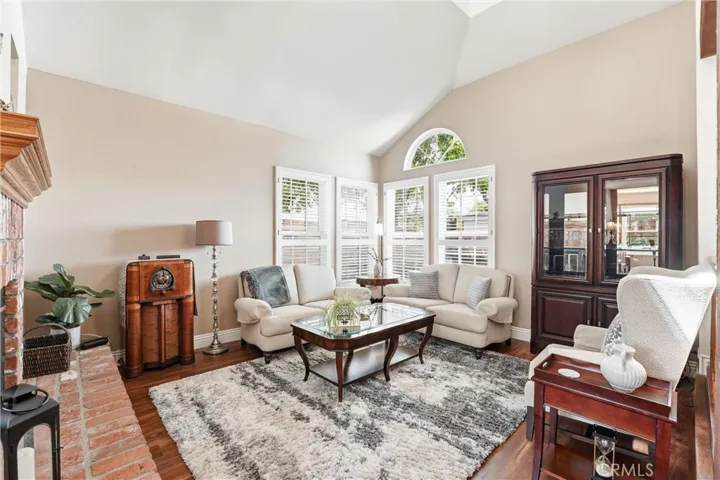 The inviting living room offers a comfortable setting for relaxing or gathering with guests, featuring oversized windows, vaulted ceilings, and views of the surrounding greenery.
