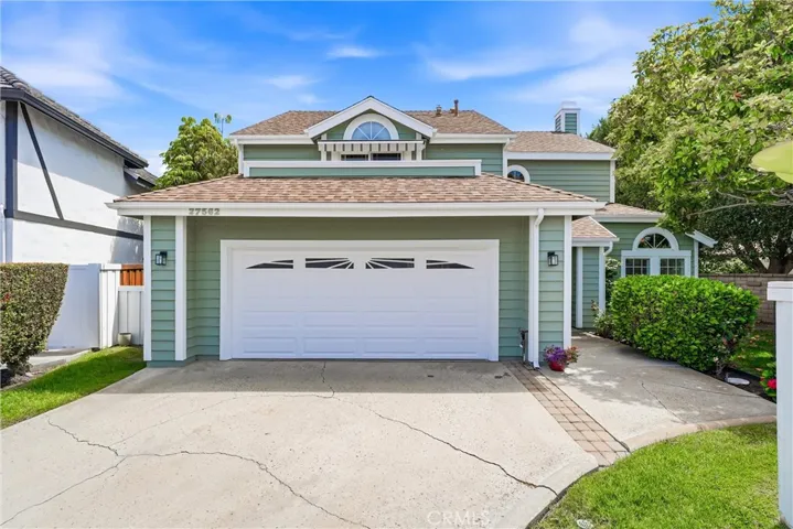 Charming coastal-inspired exterior features soft green siding, a spacious two-car garage, and mature landscaping that creates a warm first impression.