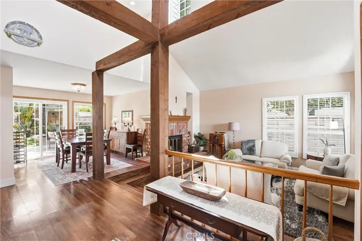 Soaring ceilings, rich wood flooring, and dramatic exposed beams create a stunning first impression in this light-filled living and dining area. Large windows and sliding doors invite natural light throughout the space.