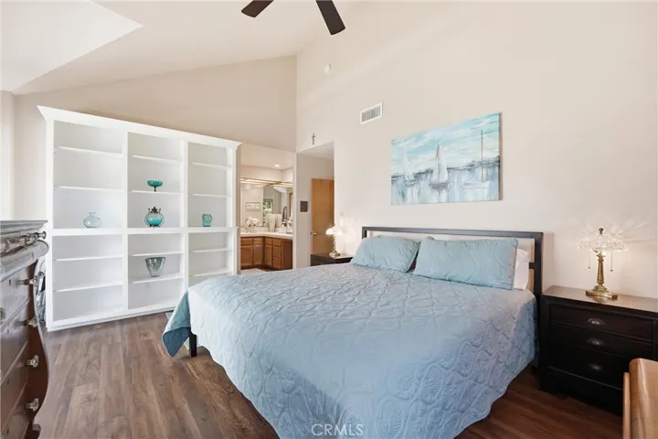 Another view of the primary suite highlights the generous room size, attractive flooring, and built-in shelving. High ceilings add to the open and inviting feel.