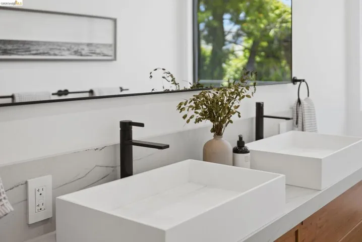 Dual rectangular vessel sinks with matte black fixtures, set on a light-toned countertop with a stone-finish backsplash